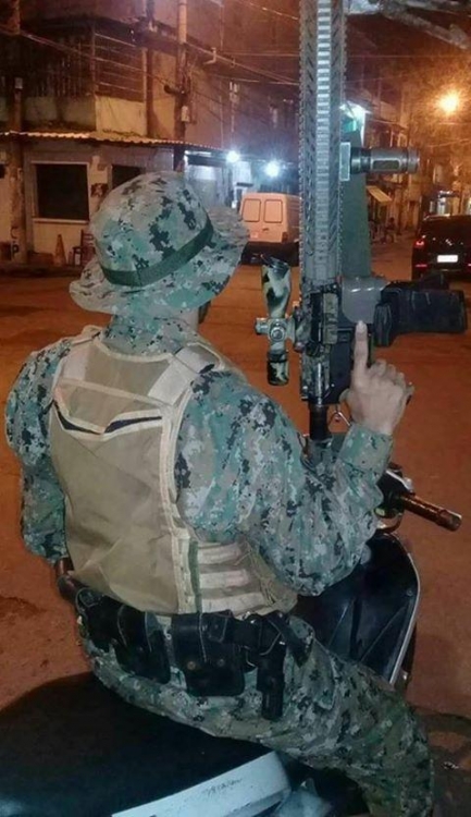 Homem segura fuzil com mira telesc&oacute;pica e carregador em cruz