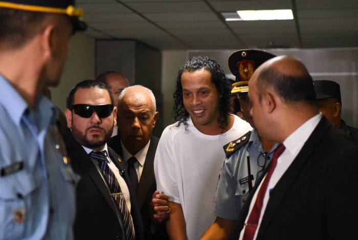 Ronaldinho (alto) vai permanecer preso. Embaixo, fã exibe bola autografada por R10, antes da prisão