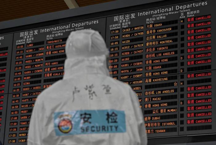 Um funcionário da segurança de aeroporto acompanha tela que mostra partidas internacionais no Aeroporto Internacional Pudong de Xangai