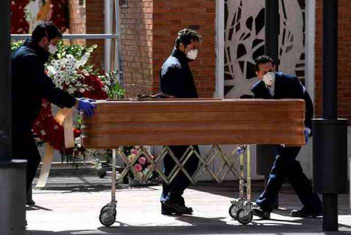 Funcionários de funerária carregam caixão para cemitério em Madri