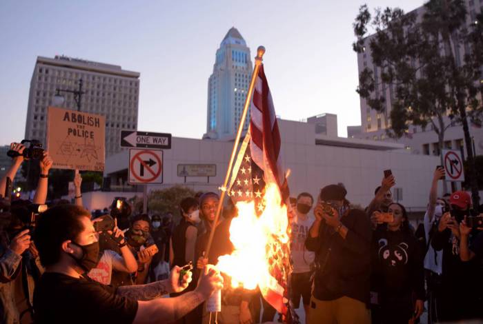 Um homem queimou uma bandeira de cabeça para baixo dos EUA quando manifestantes se reuniram no centro de Los Angeles em 27 de maio de 2020 para se manifestar depois que George Floyd