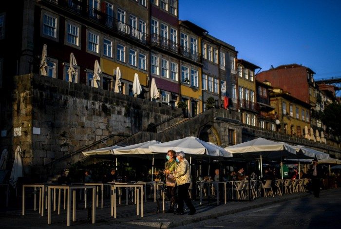 Two women wearing face masks walk at Ribeira in downtown Porto on October 21, 2020. - Portugal, which locked down comparatively early to avoid the worst excesses of the first wave of the coronavirus pandemic, has in recent weeks been battling a rising caseload. (Photo by PATRICIA DE MELO MOREIRA / AFP)