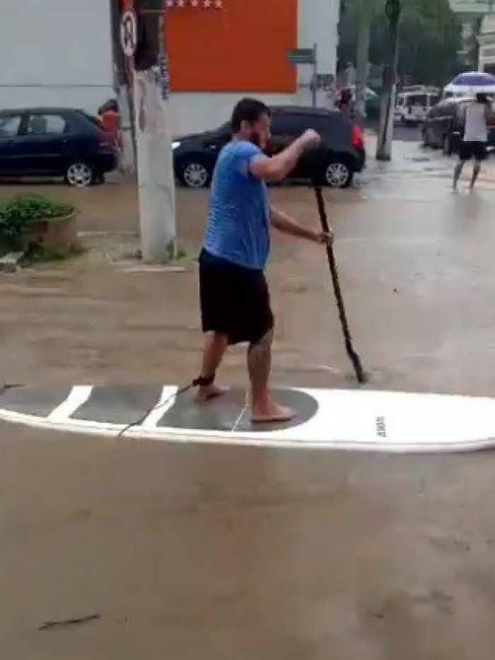 Homem improvisa prancha e remo para fugir de alagamento - Twitter / Reprodução 