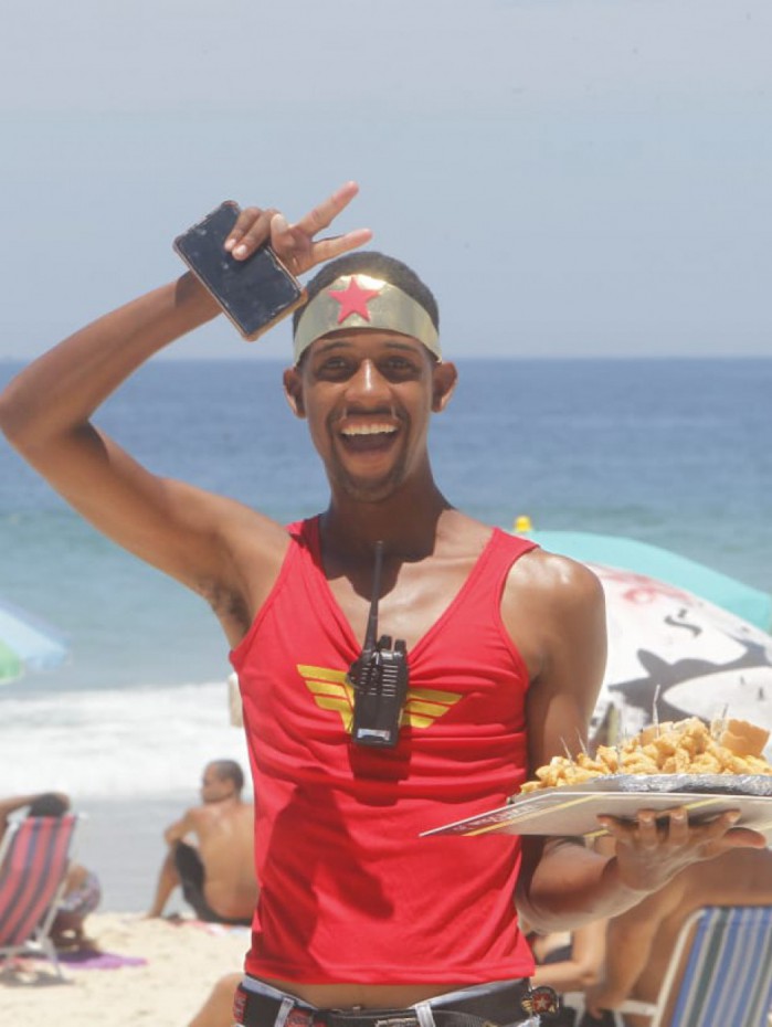 Com sorriso no rosto e sol na cabe&ccedil;a, vendedor trabalha na areia da Barra
