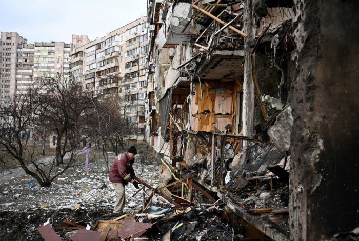 Homem limpa destroços em um prédio residencial danificado na rua Koshytsa, subúrbio de Kiev