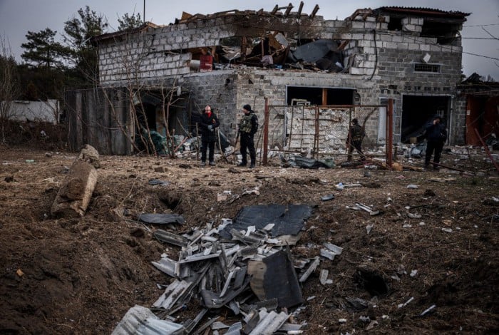 Policiais e moradores ao lado de uma cratera em frente a uma casa danificada por bombardeios recentes, nos arredores de Kiev, na Ucrânia, neste sábado (12)