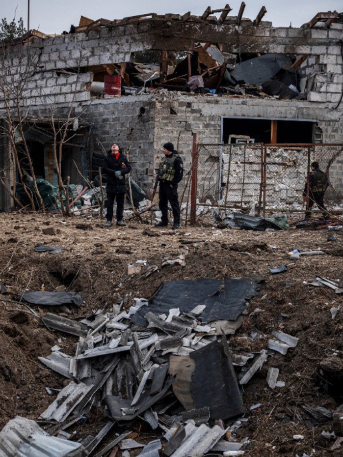Policiais e moradores ao lado de uma cratera em frente a uma casa danificada por bombardeios recentes, nos arredores de Kiev, na Ucrânia, neste sábado (12)