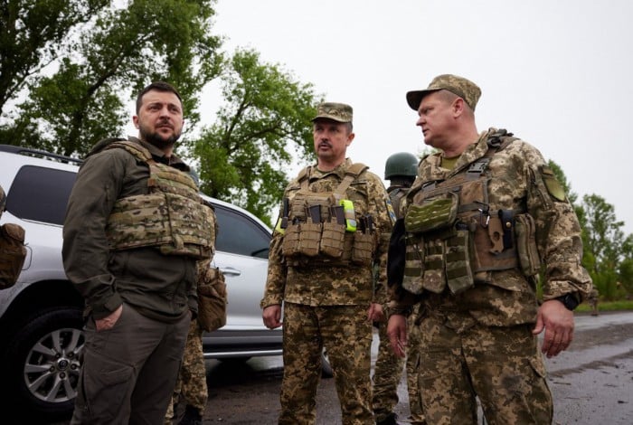 Volodymyr Zelensky usando colete à prova de balas acompanhados por soldados ucranianos