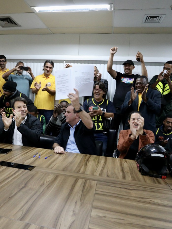 Eduardo Paes exibe o texto, enquanto alguns pilotos vibram com o início do processo de legalização