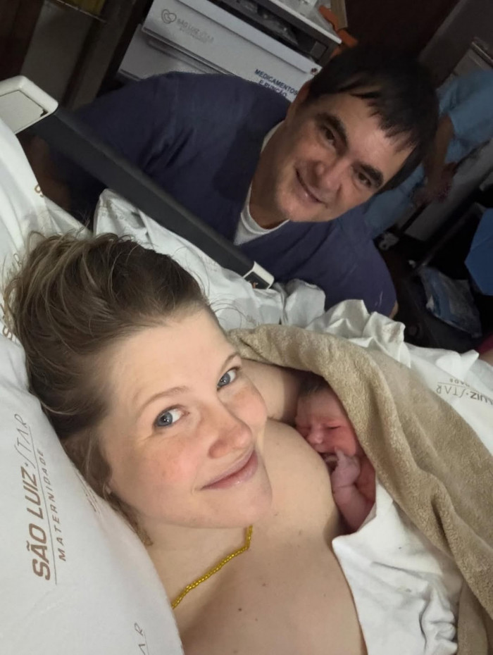 Samuel Rosa ao fundo e Laura Sarkovas com Dora em seus braços.